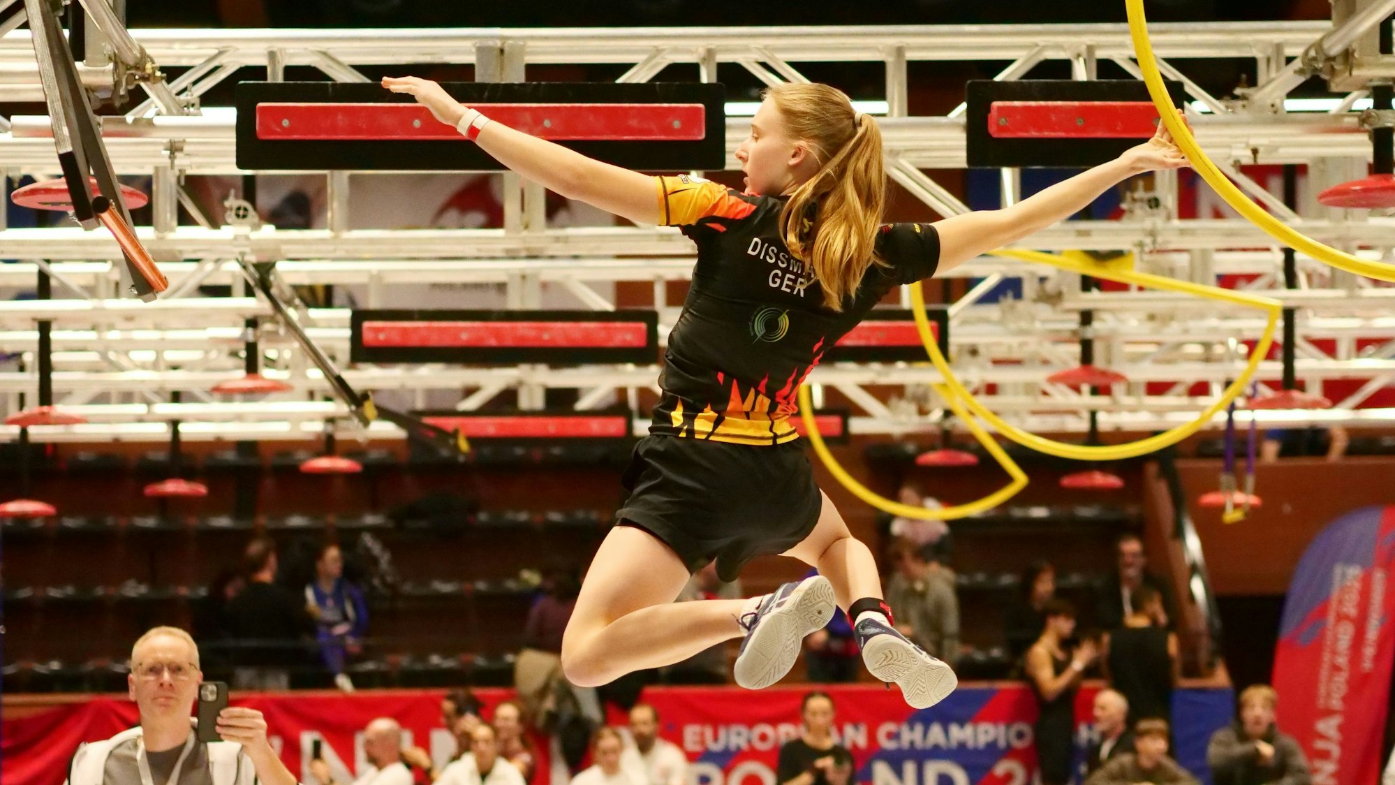 Szene aus dem Ninja-Sport, eine junge Frau hangelt durch einen Hindernisparcours.