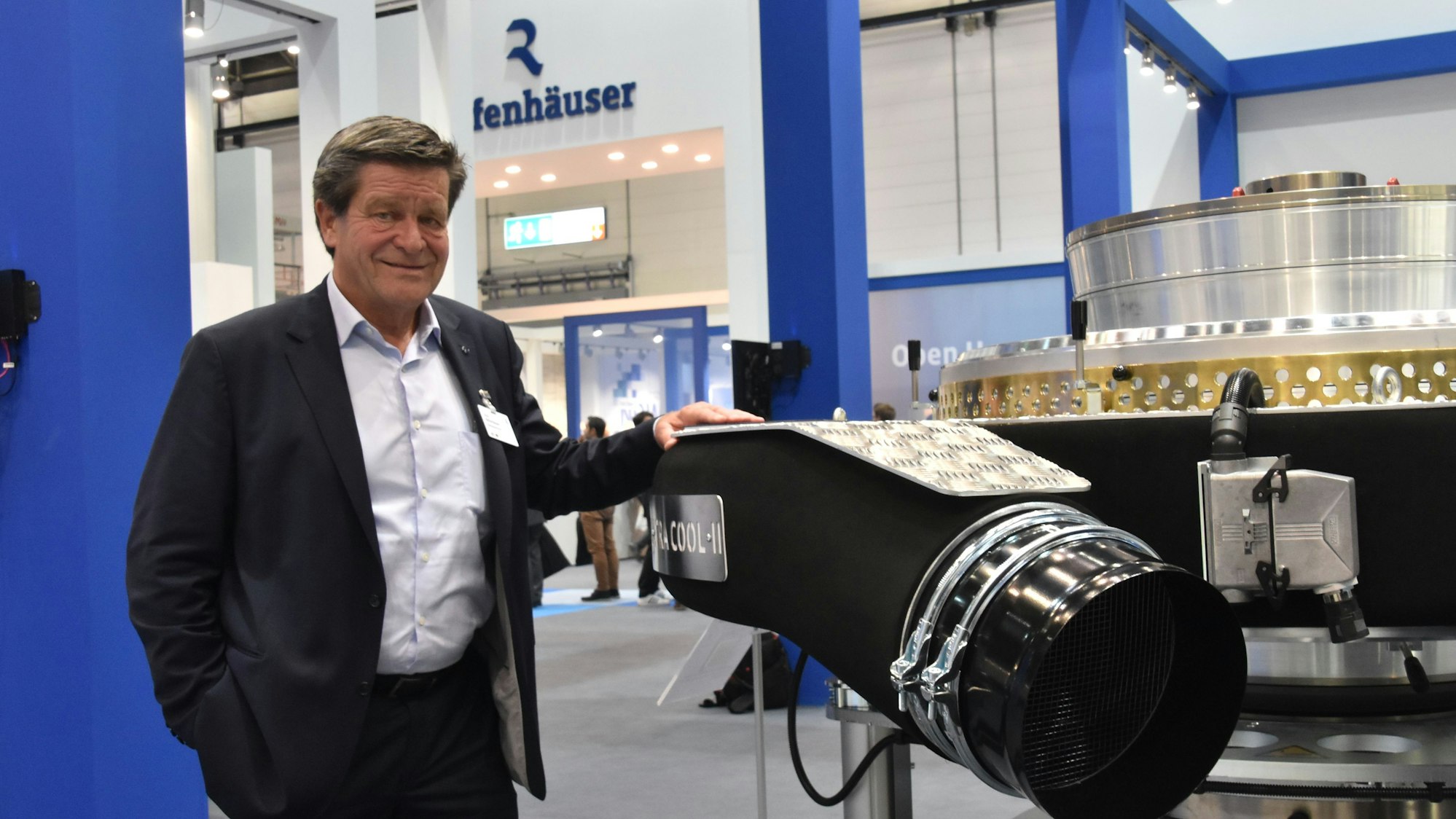 Ein Mann im Anzug steht neben einer Maschine an einem Messestand.