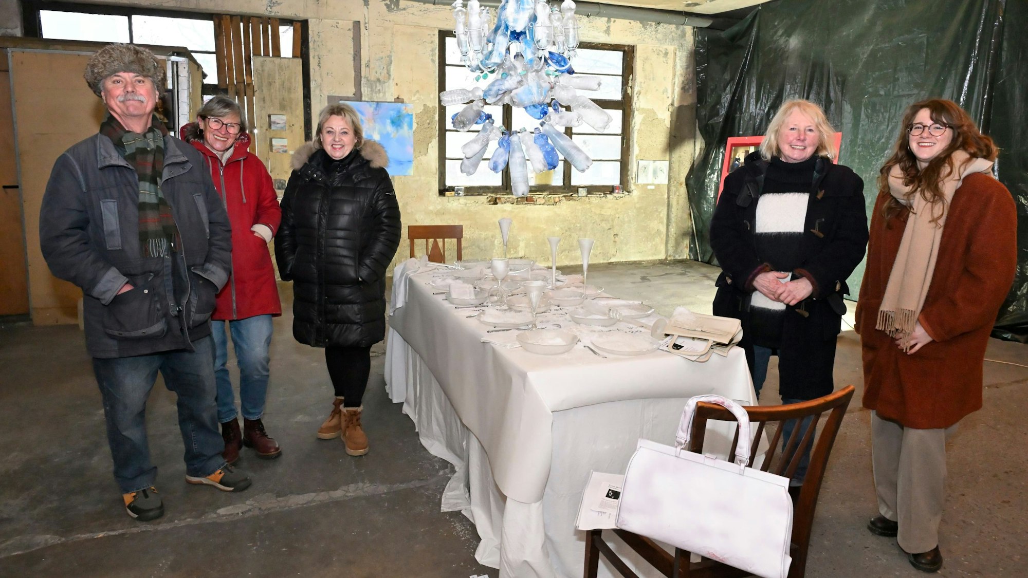Die Künstler Franz Gerd Frank, Angelika Biber, Mechtild Stroß und Waltraud Wolf und die Kölner Dichterin Lea Najork stehen um einen ganz in weiß gedeckten Tisch in den Lux-Hallen (v.l.n.r.).