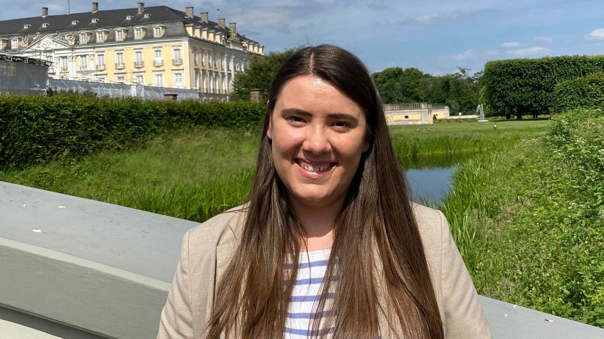 Eine junge Frau steht im Park vor dem Brühler Schloss.