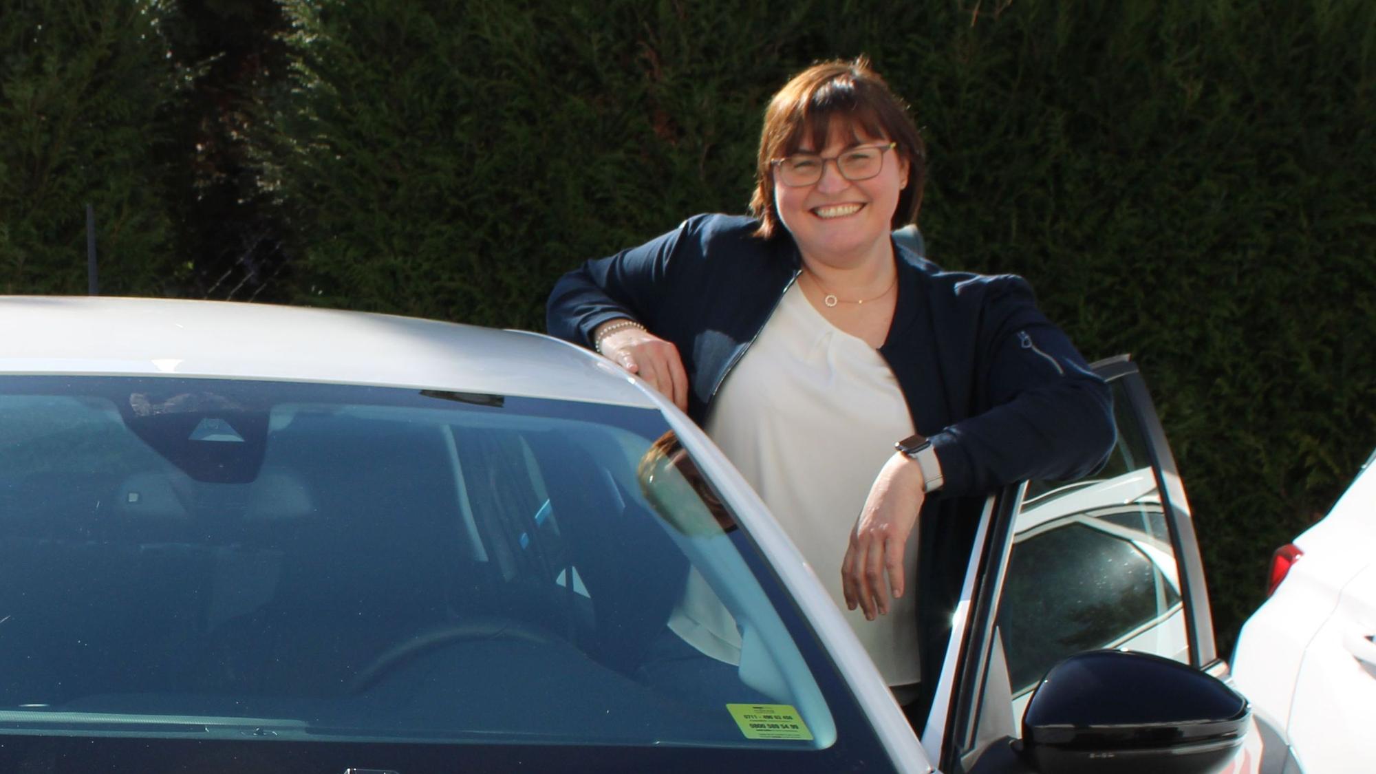 Eine Frau steht neben einem Auto hinter der geöffneten Fahrertür.