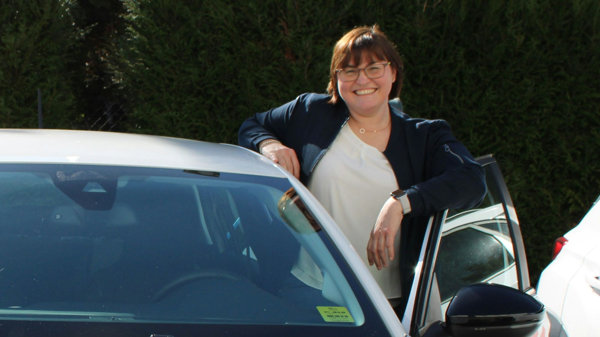 Eine Frau steht neben einem Auto hinter der geöffneten Fahrertür.