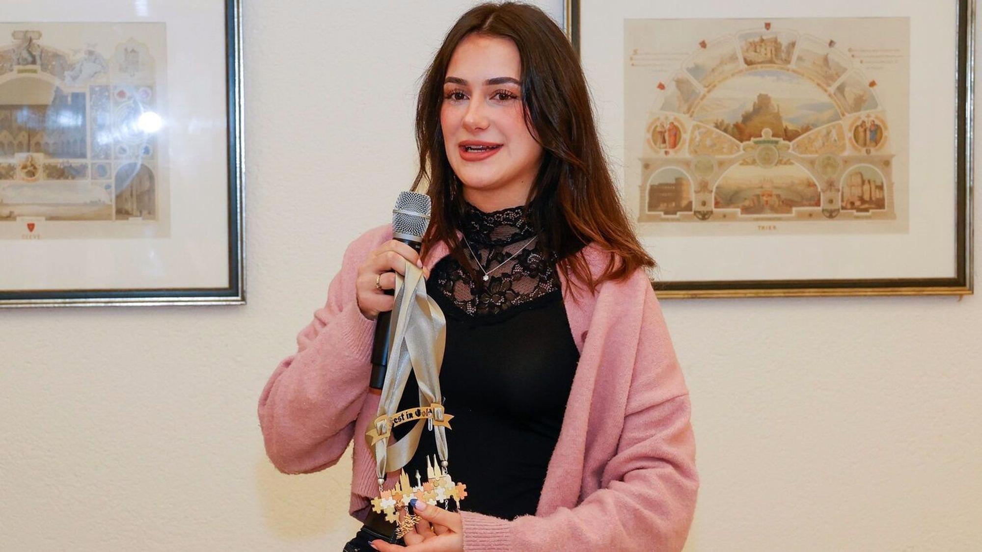 Hannah Homberg hält ein Mikrofon und ihren Orden in der Hand.