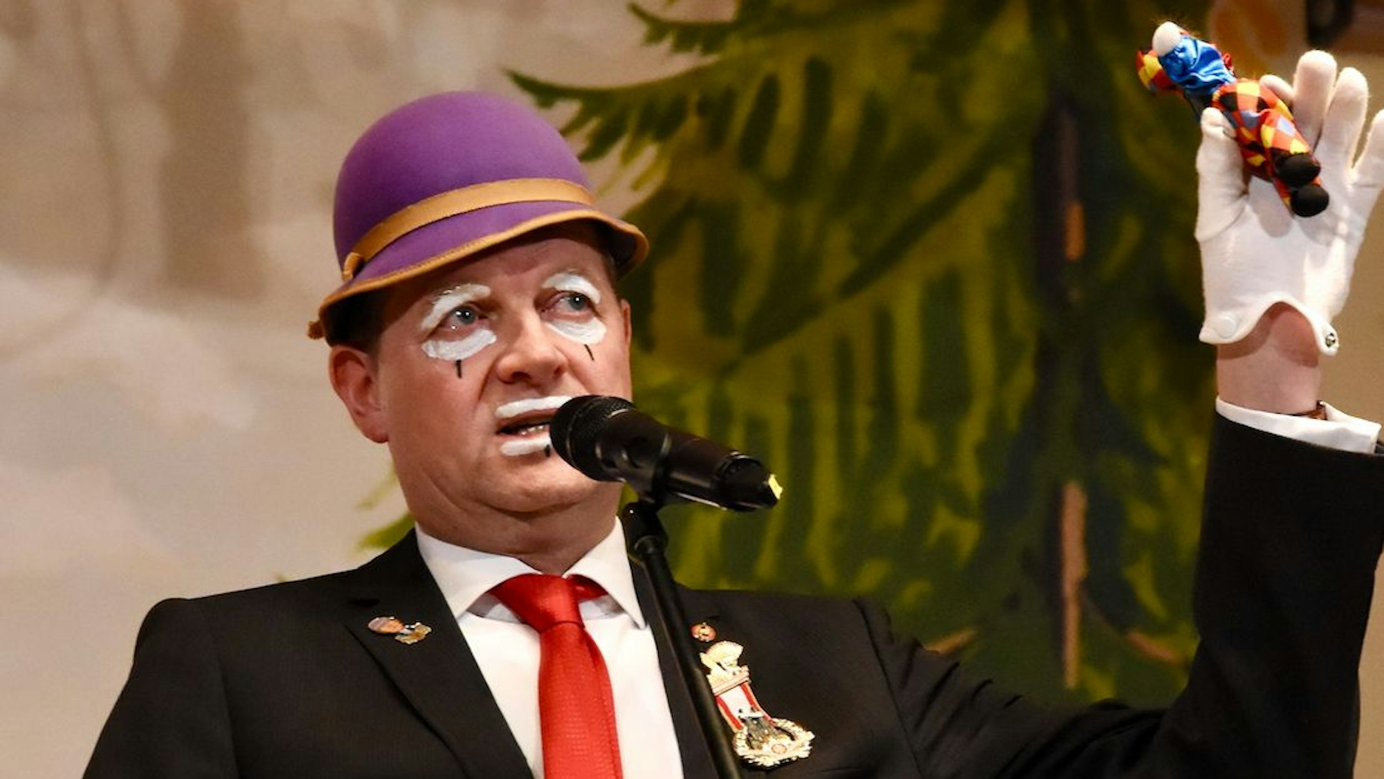 Boris Müller steht auf der Bühne vor einem Mikro und hebt die Hand.