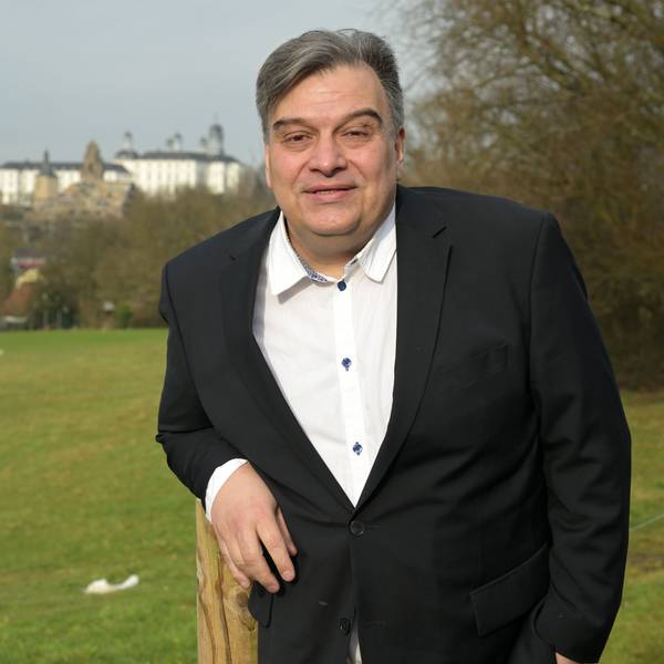 Ein Mann steht vor einer grünen Wiese, im Hintergrund sieht man das Bensberger Schloss.