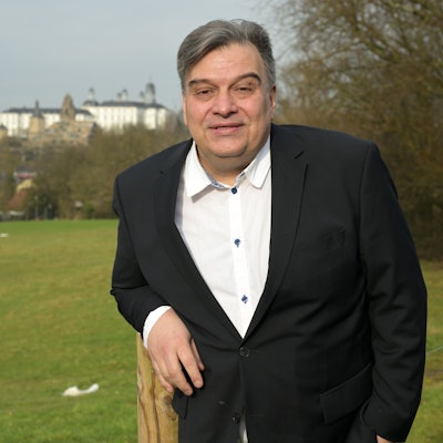 Ein Mann steht vor einer grünen Wiese, im Hintergrund sieht man das Bensberger Schloss.