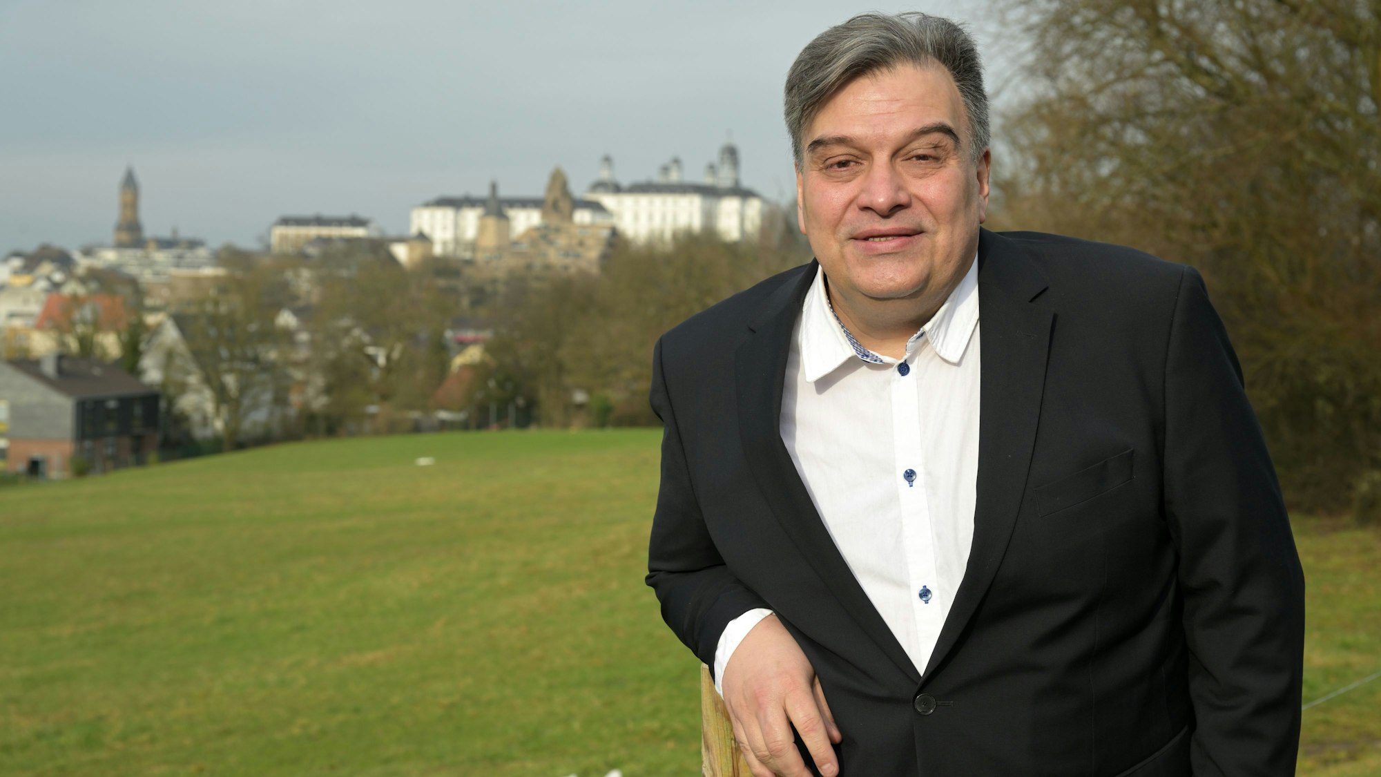 Ein Mann steht vor einer grünen Wiese, im Hintergrund sieht man das Bensberger Schloss.