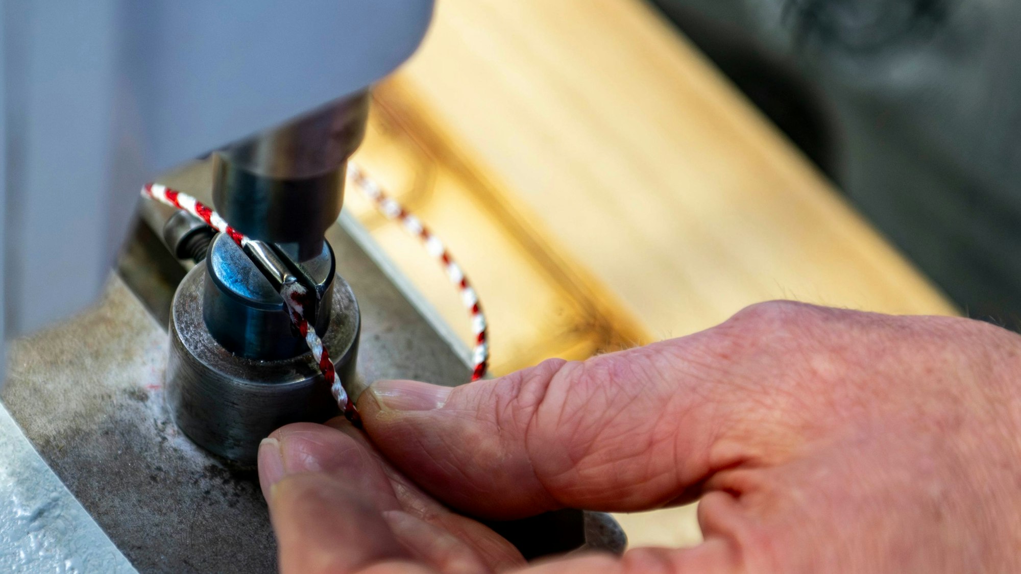 An einer Maschine wirden die beiden Enden der rot-weißen Schnur eines Ordens mit einer Hülse verbunden.