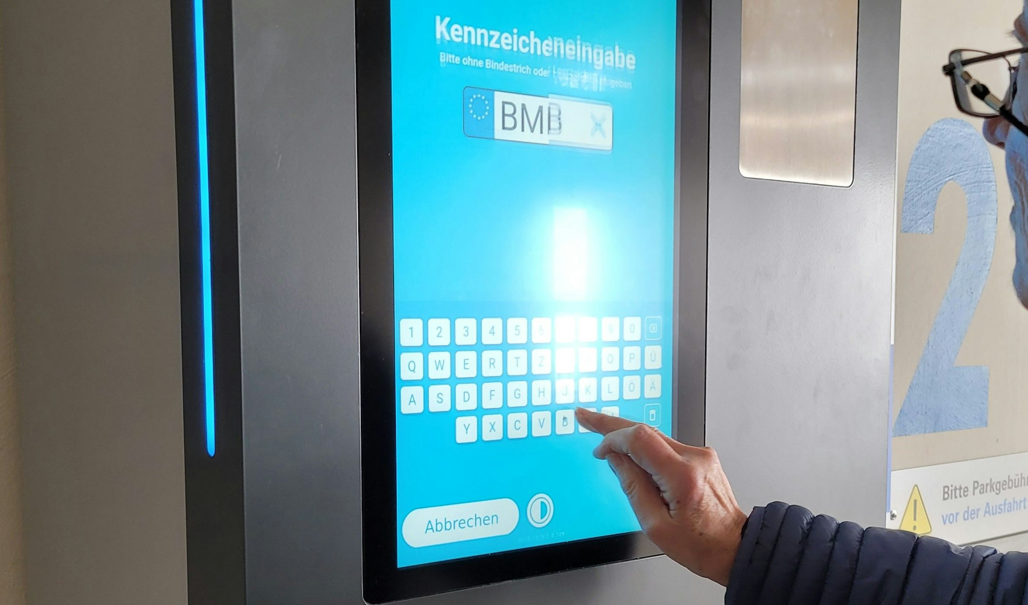 Ein Parkautomat, zu sehen sind ein Buchstabenfeld und ein Hand.