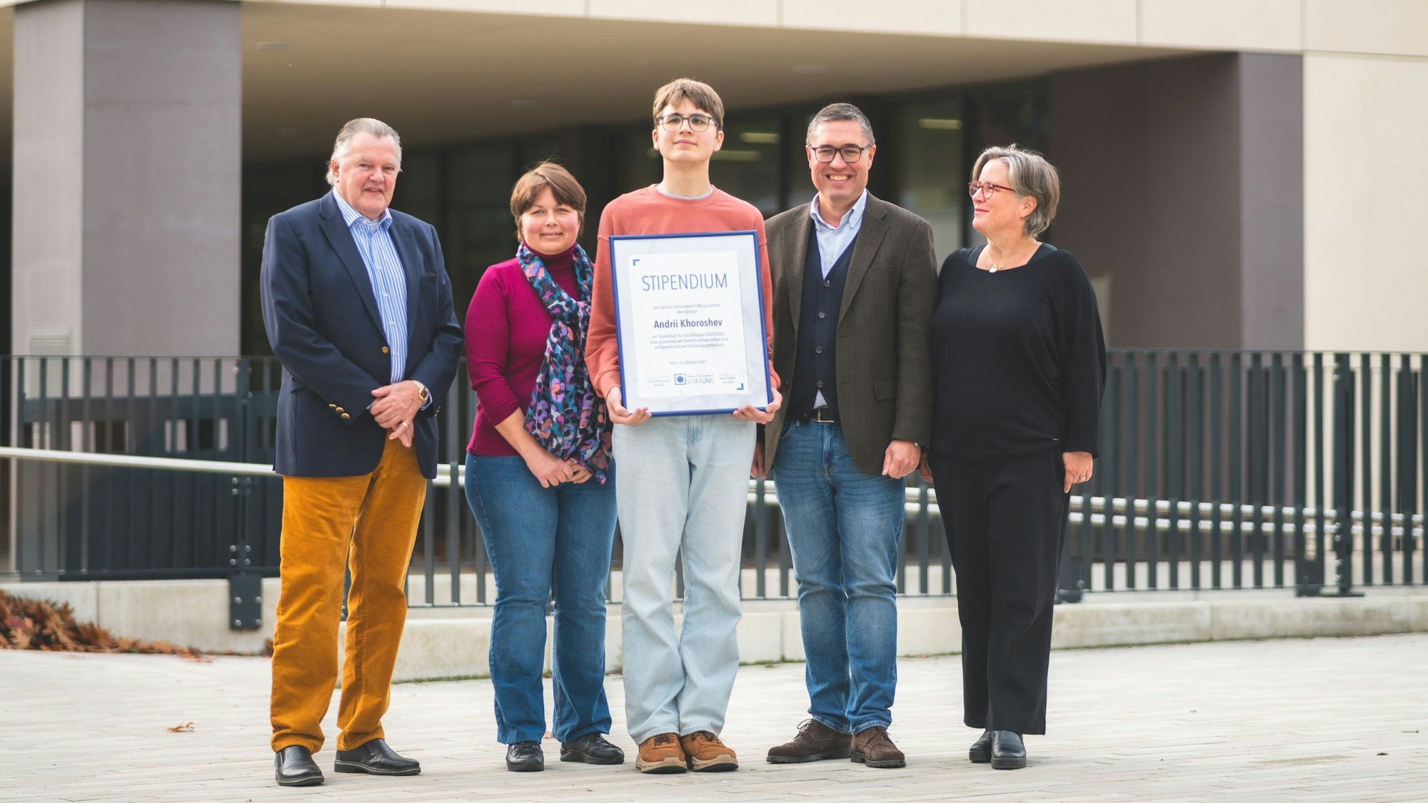 Fünf Personen stehen nebeneinander auf einem Gruppenbild vor dem Schuleingang.