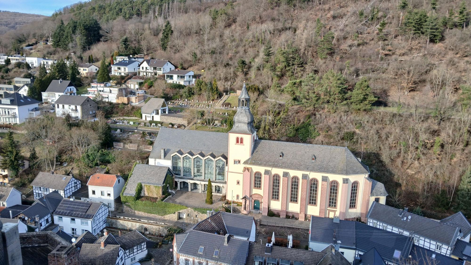 Das Bild zeigt die von Häusern umgebene Kirche und im Hintergrund Wald.