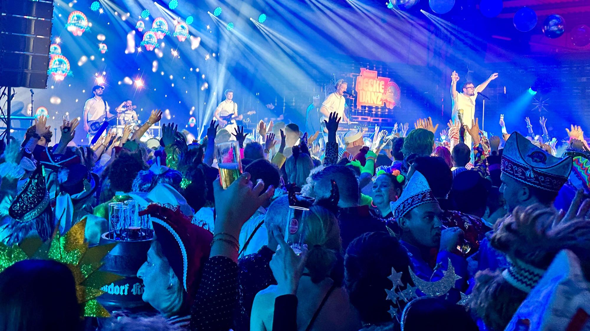 Eine Band animiert das feiernde Publikum auf einer Bühne.