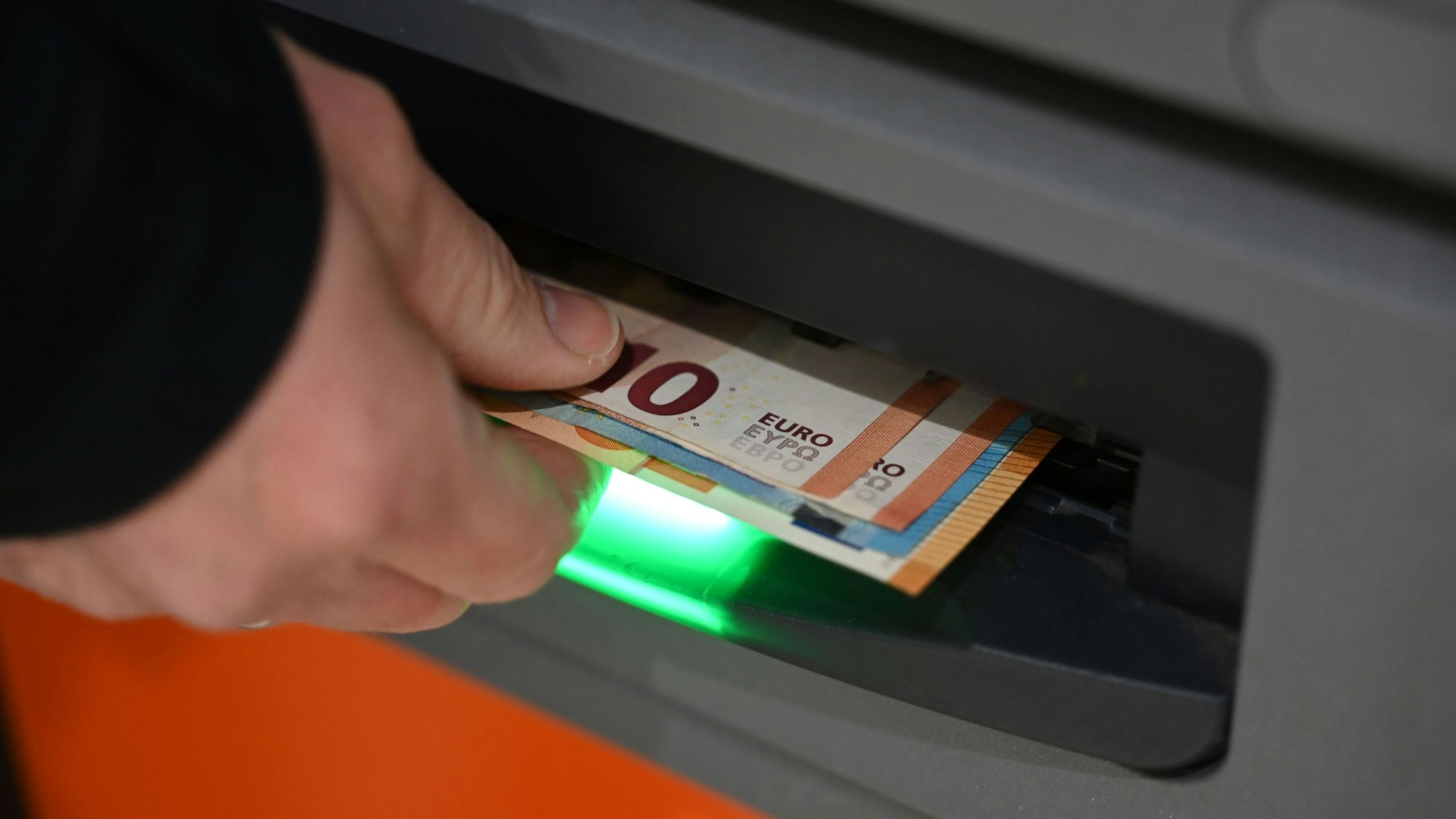 Eine Hand greift nach Banknoten, die aus dem Ausgabeschlitz des Automaten kommen.
