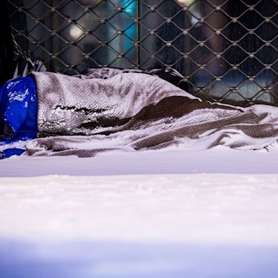 Das Foto zeigt einen Menschen, der im Schnee auf der Straße schläft.