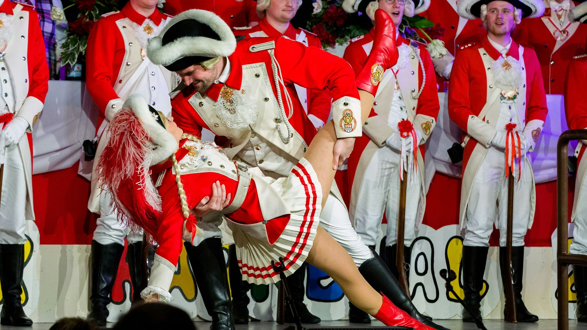 Auf einer Bühne stehen Mitglieder einer Karnevalsgesellschaft, im Vordergrund ein Tanzpaar in Aktion.