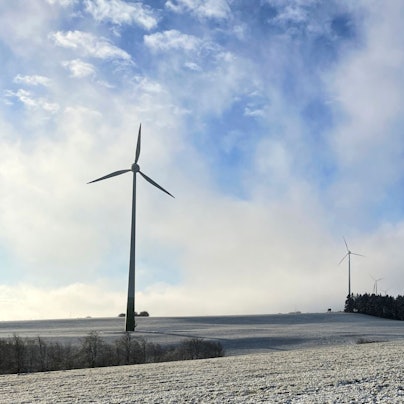Windräder im Hellenthaler Höhengebiet bei Oberreifferscheid stehen auf einer verschneiten Wiese.