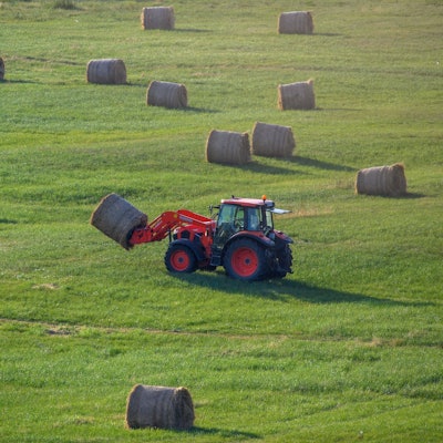 Ein roter Tracktor fährt mit einem Heuballen über eine grüne Wiese.