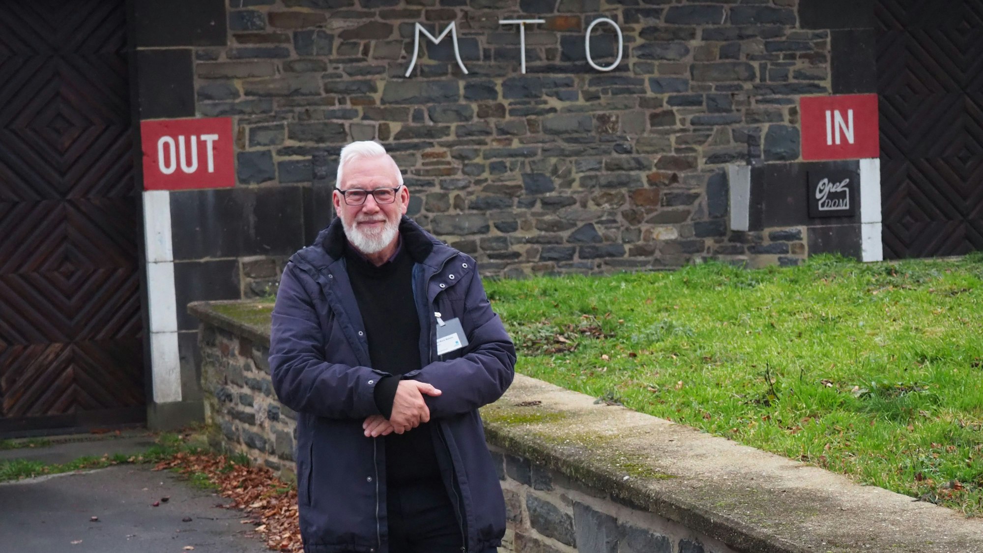 Jean-Marie Malaise, mit weißem Bart und einer blauen Jacke, steht vor einem Gebäude mit der Aufschrift MTO.
