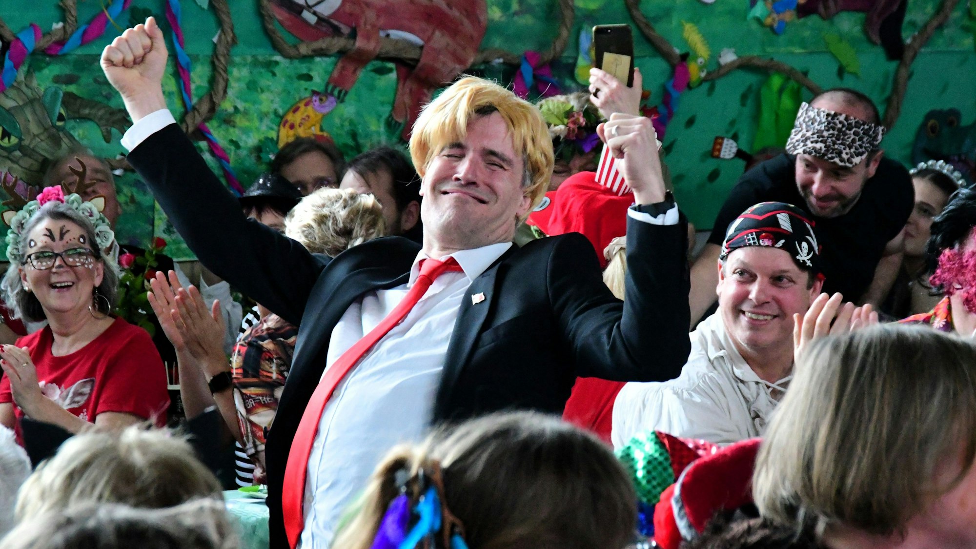 Ein als Donald Trump verkleideter Mann steht in Angeberpose zwischen den Besuchern.