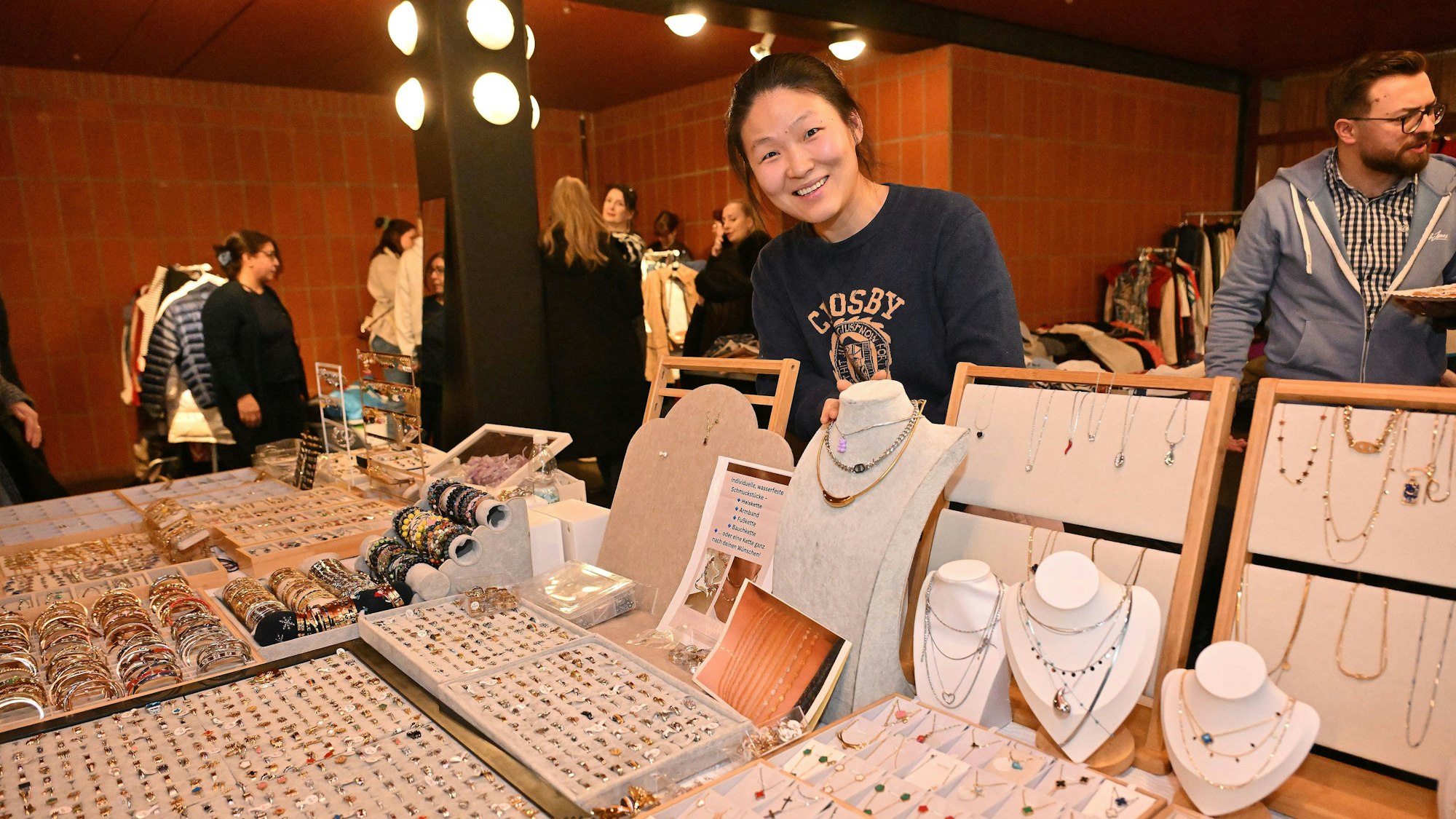 Eine Frau steht hinter einem Stand, auf dem sich verschiedene Schmuckstücke befinden.