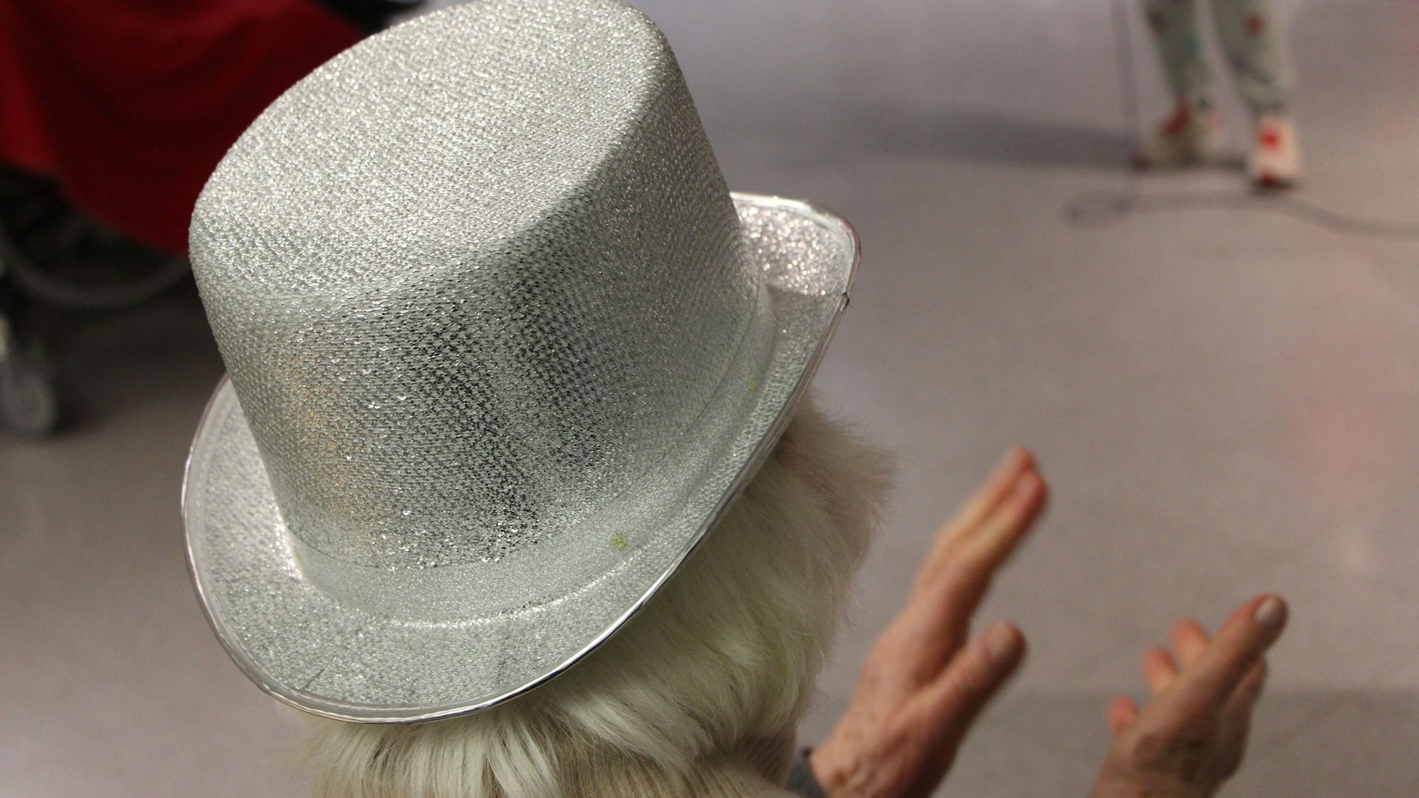 Eine Frau mit weißen Haaren und silbernem Hut, von hinten, applaudiert
