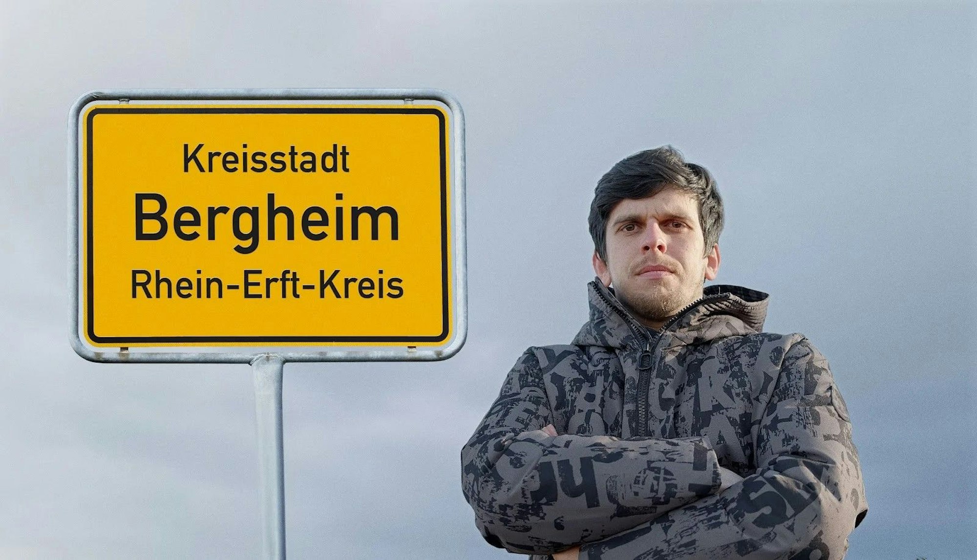 Auf dem Foto steht ein Mann mit verschränkten Armen vor einem Ortsschild der Stadt Bergheim.