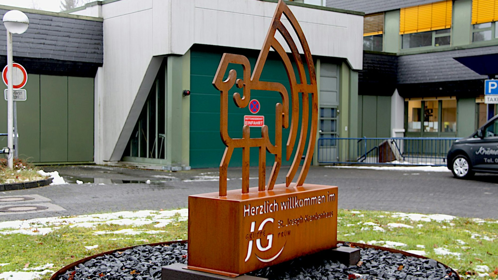Eine Statue mit dem Logo des Krankenhauses Prüm steht vor der Klinik.