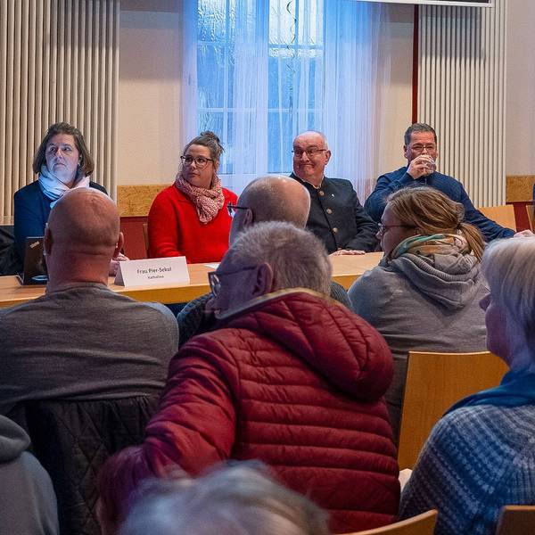 Foto einer Frau, die vor einer Bürgerversammlung spricht.