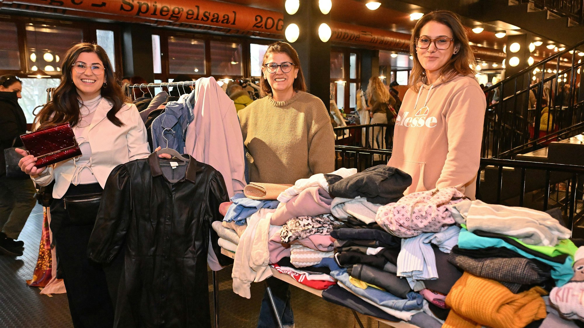 Drei Frauen stehen hinter einem Stand mit Kleidung.