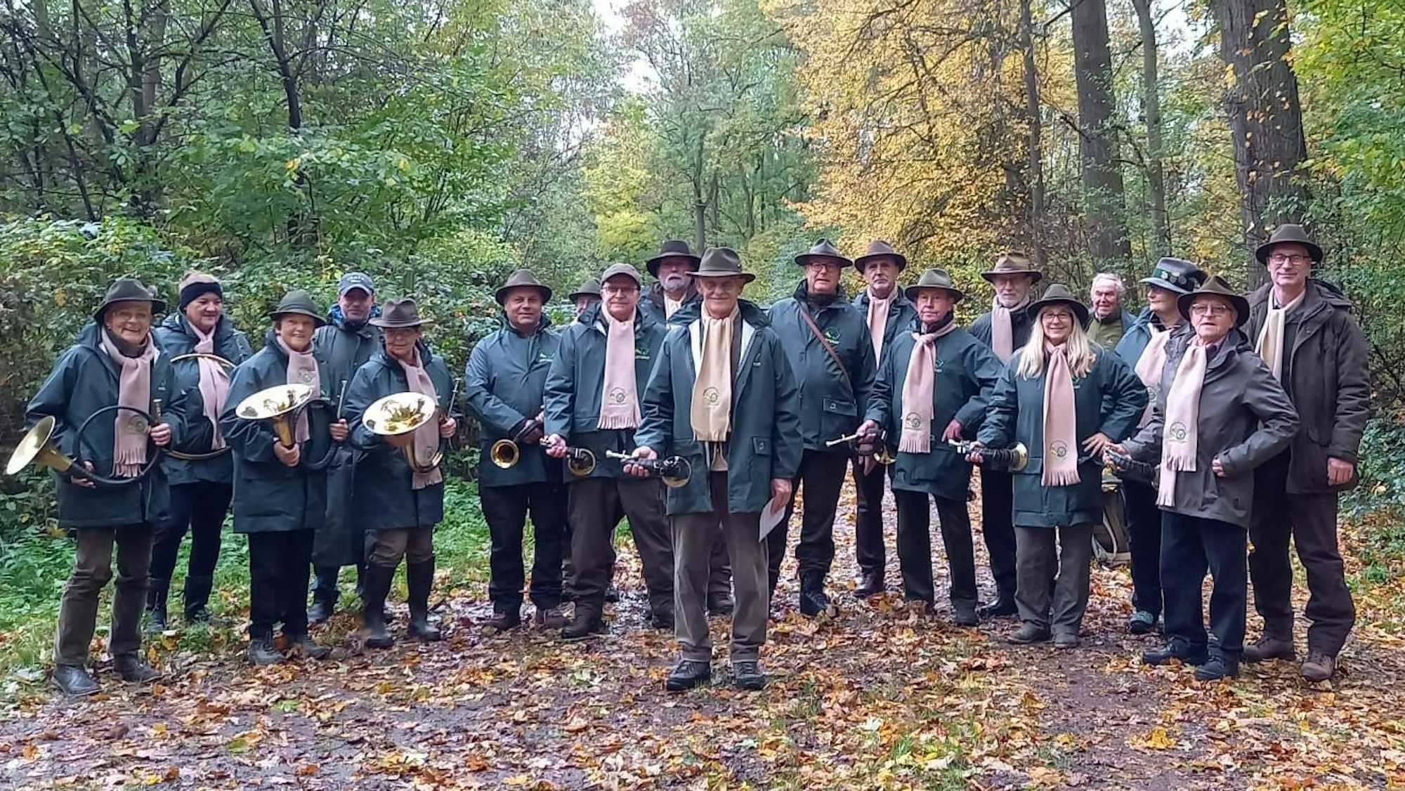 Ein Korps aus Jagdhornbläsern steht im Wald und hat die Hörner in den Händen.