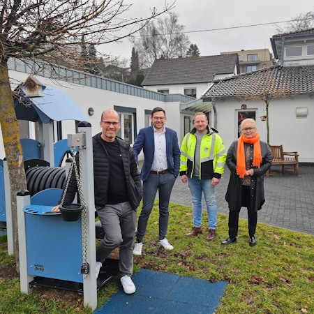 Drei Männer und eine Frau stehen an einem Spielgerät im Außenbereich der Kita Kallbachstraße in Kall.