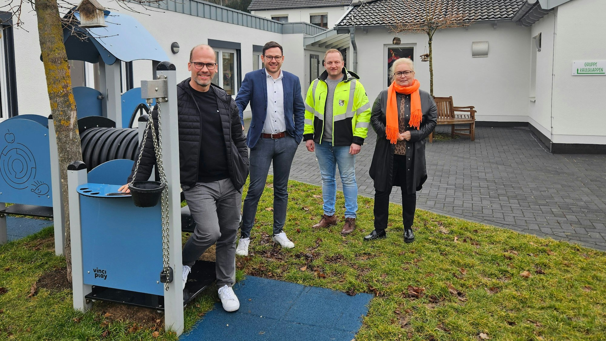 Drei Männer und eine Frau stehen an einem Spielgerät im Außenbereich der Kita Kallbachstraße in Kall.