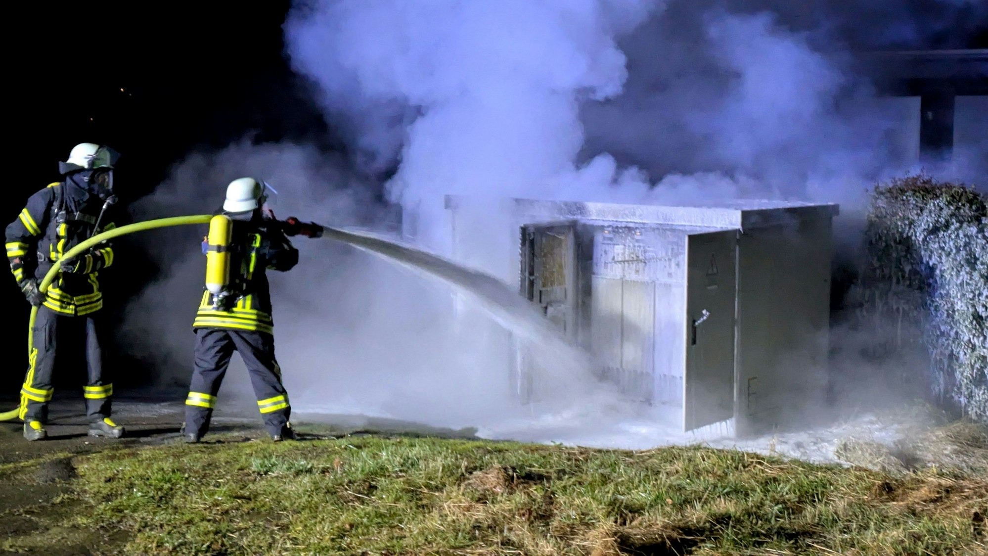 Zwei Feuerwehrleute löschen einen brennenden Trafo in der Bergstraße in Nettersheim mit Schaum.
