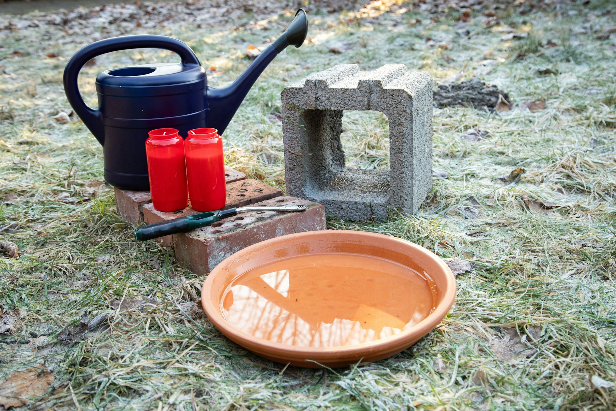 Man braucht: Ziegelsteine, einen Pflanzstein, einen Blumenuntersetzer und Grablichter.