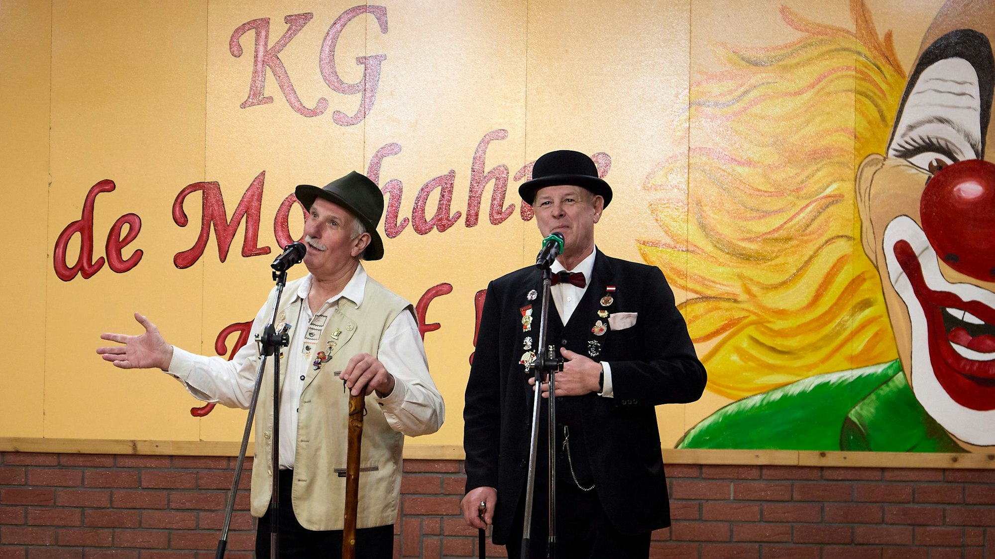 Zwei Redner stehen in Kostümen auf der Bühne.