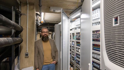 Ein Mann mit Vollbart steht in einem Raum voller Technik.