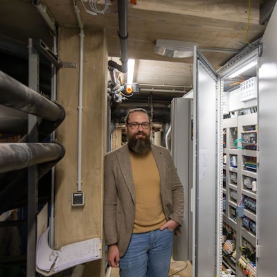 Ein Mann mit Vollbart steht in einem Raum voller Technik.