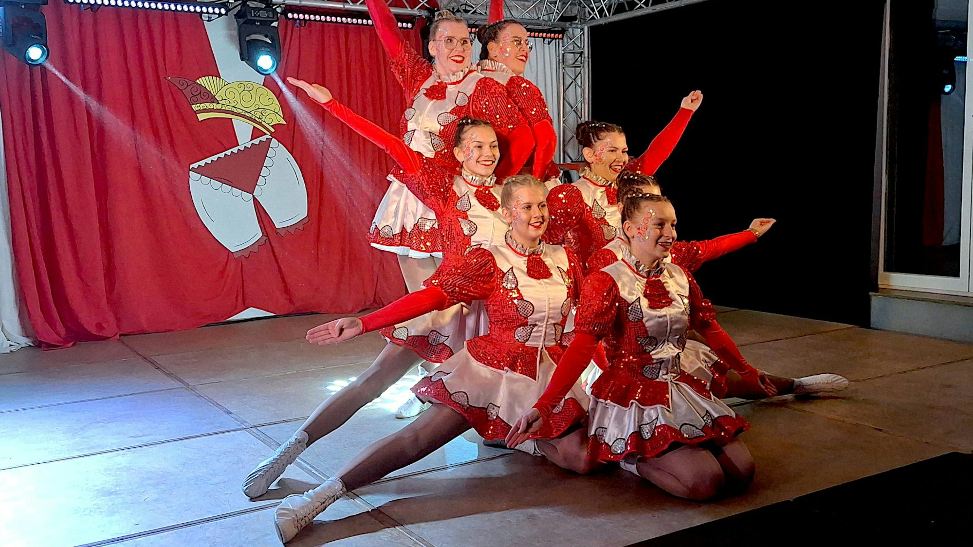 Zwei Frauen und fünf Mädchen haben sich zu einer Bühnenfigur mit ausgestreckten Armen positioniert.