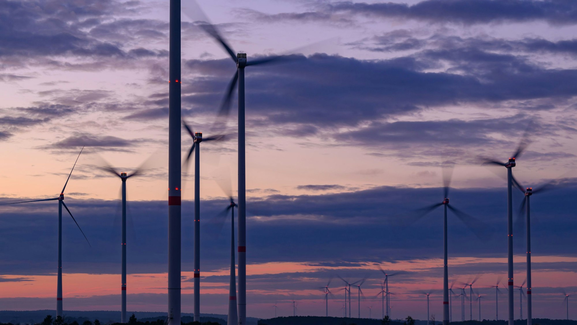 Das Symbilbild zeigt den am frühen Morgen leuchtenden Himmel über Windenergieanlagen.