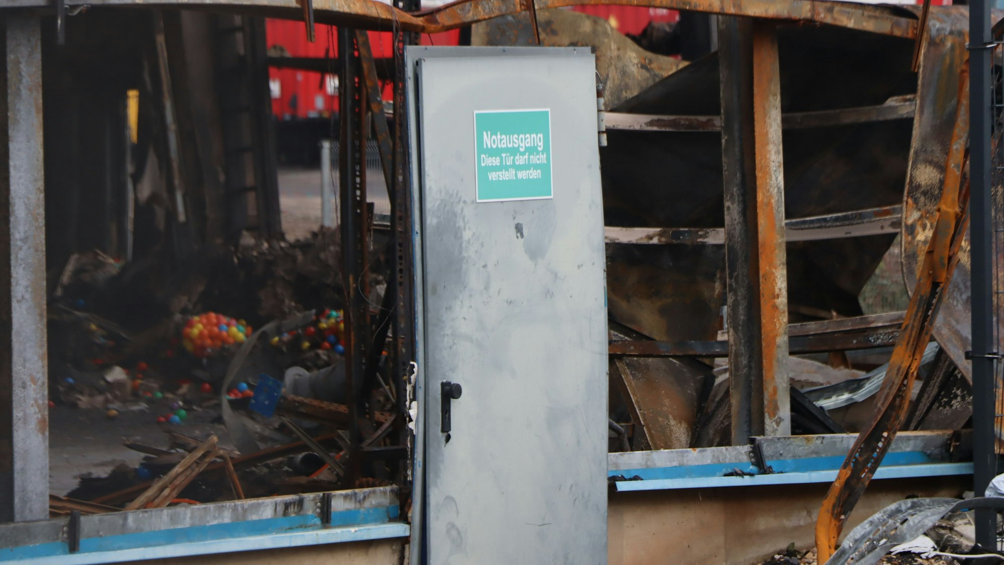 Zu sehen ist eine Metalltür, die sich in der Hitze eines Brandes verformt hat.