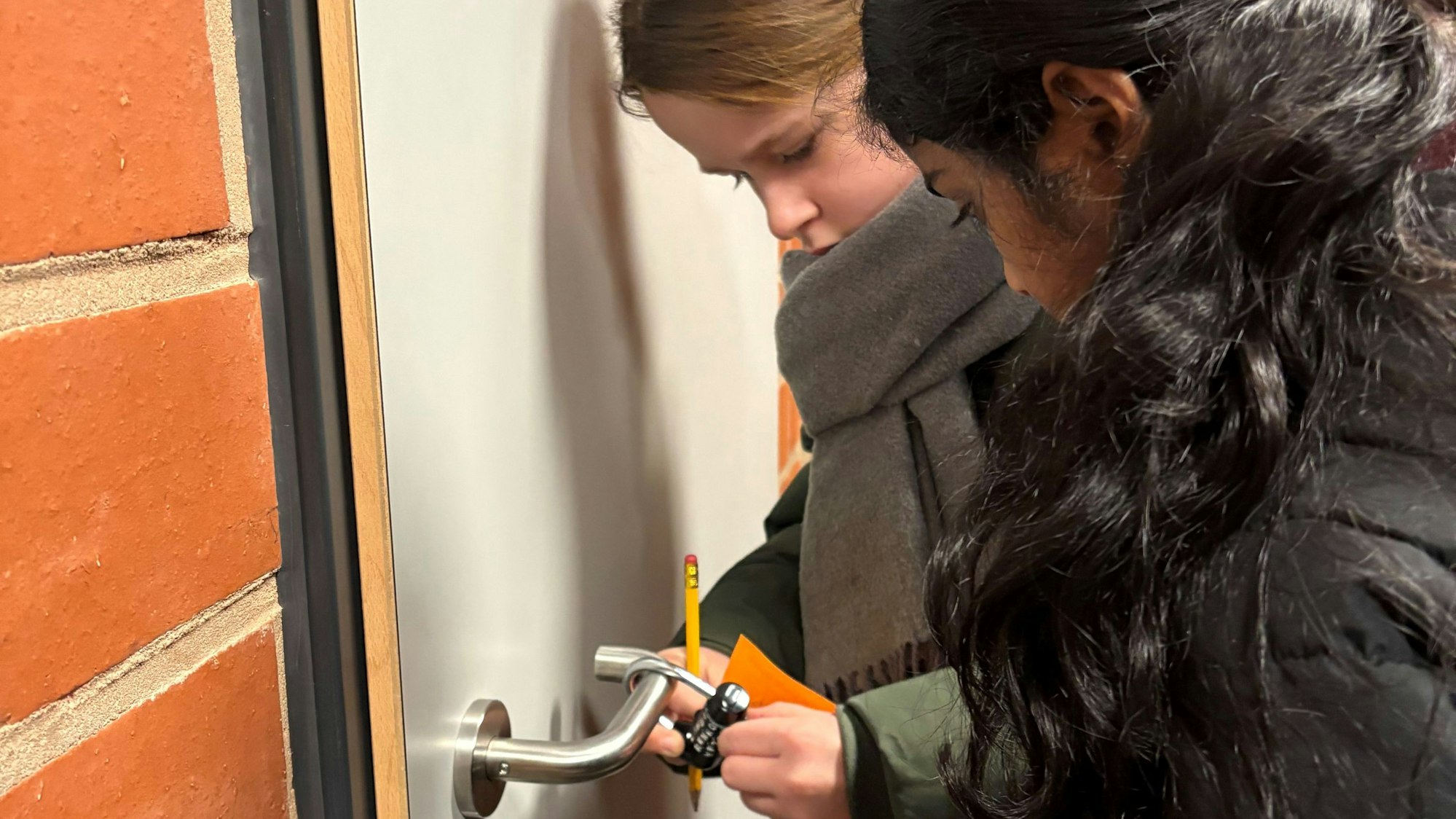 An der Tür hängt ein Buchstabenschloss. Zwei Grundschülerinnen geben das Codewort „Lesen“ ein.