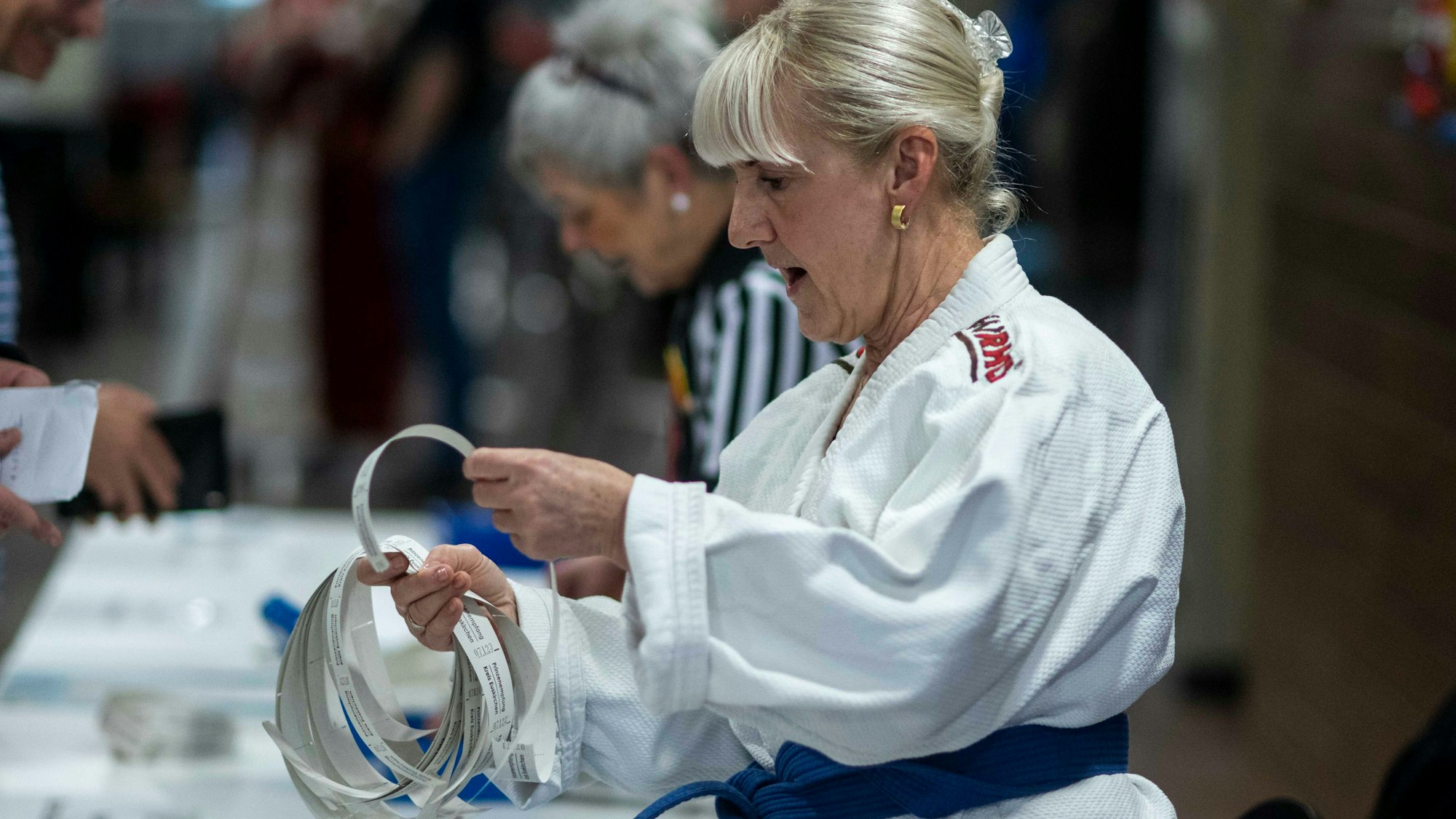 Eine Frau im Judoanzug bei der Ausgabe von Getränke-Wertmarken aus Papier.