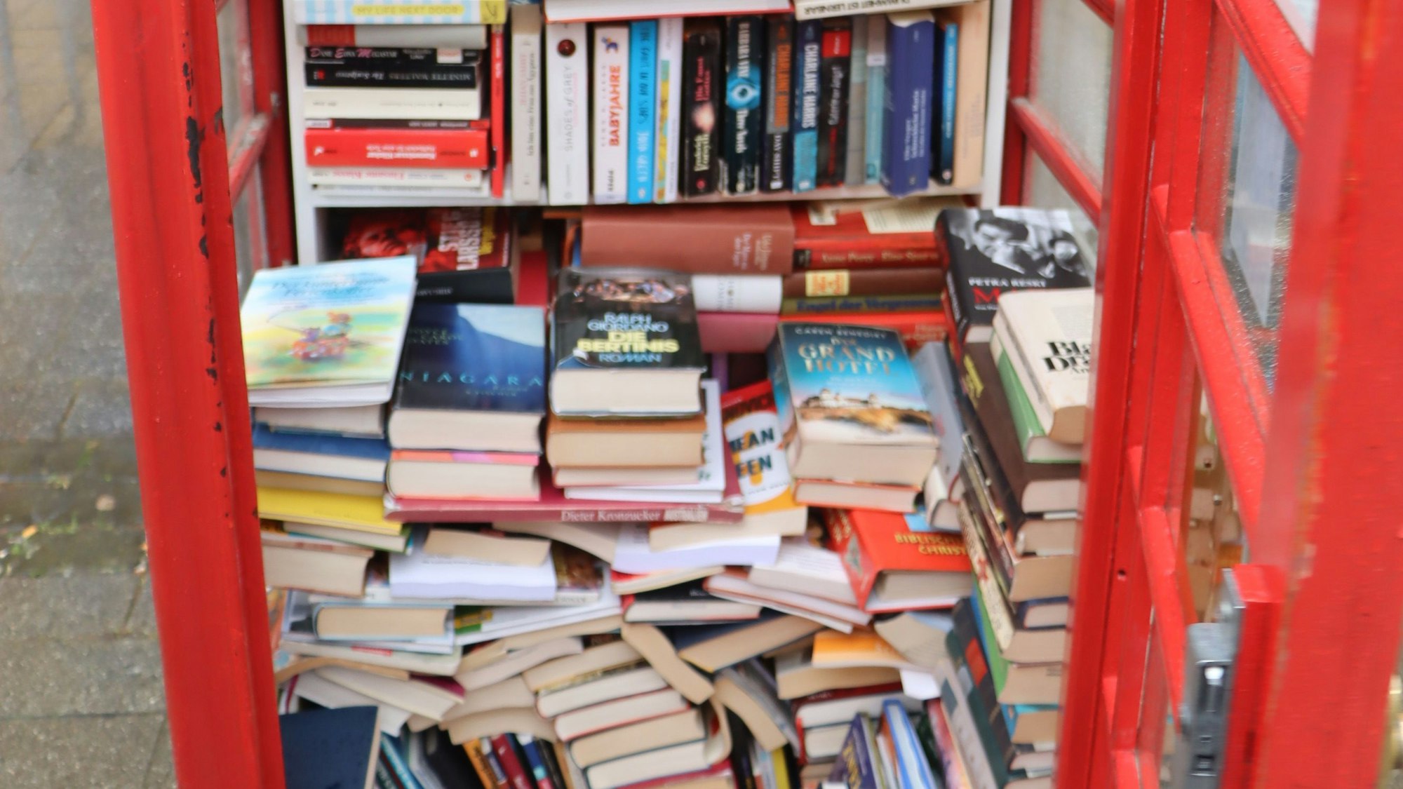 Zu sehen ist ein Bücherschrank, in dem Unmengen an Büchern gestapelt werden.