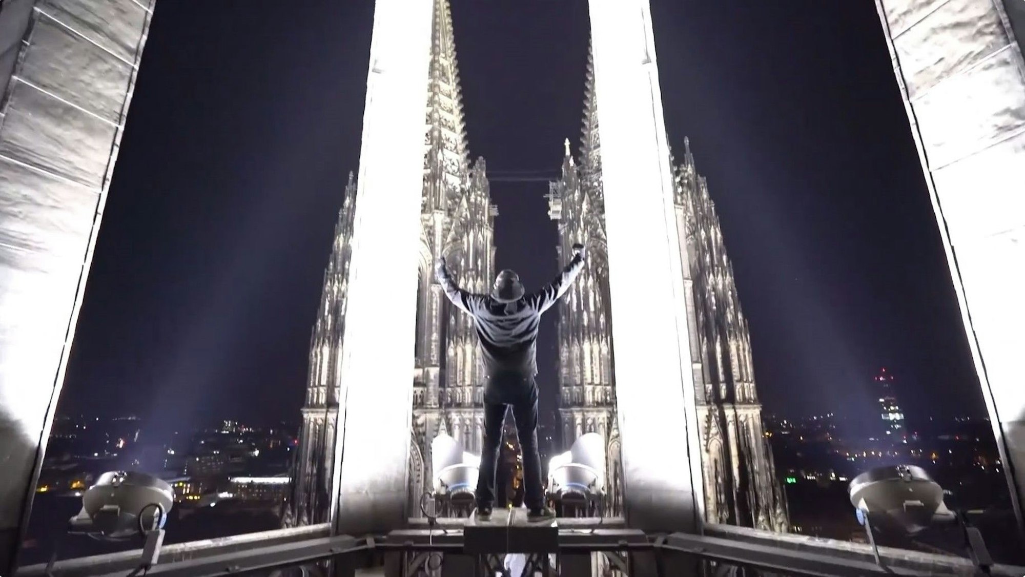 Ein Screenshot aus dem YouTube-Video der Gruppe. Ein Mitglied steht auf einem Gerüst des Nordturms und streckt die Arme triumphierend in die Luft.