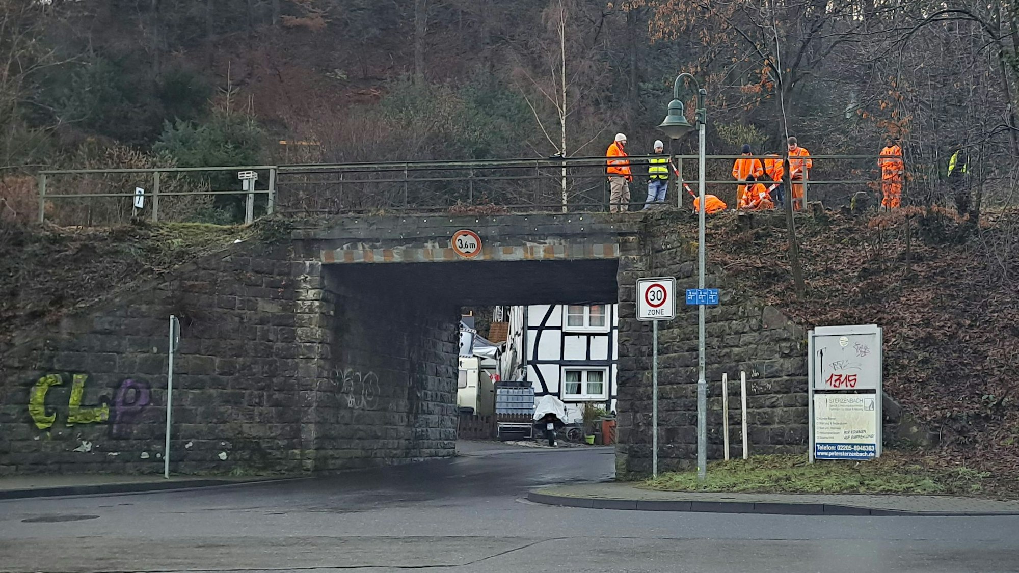 Menschen in orangefarbener Warnkleidung stehen auf der zu erneuernden Bahnbrücke über die Lüghauser Straße in Rösrath-Hoffnungsthal.
