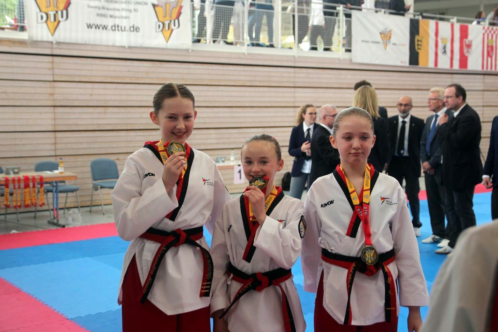 Alexandra Simin (l.) vom Taekwondo-Club Schleiden steht neben zwei anderen Sportlerinnen und hält eine Medaille in die Kamera.