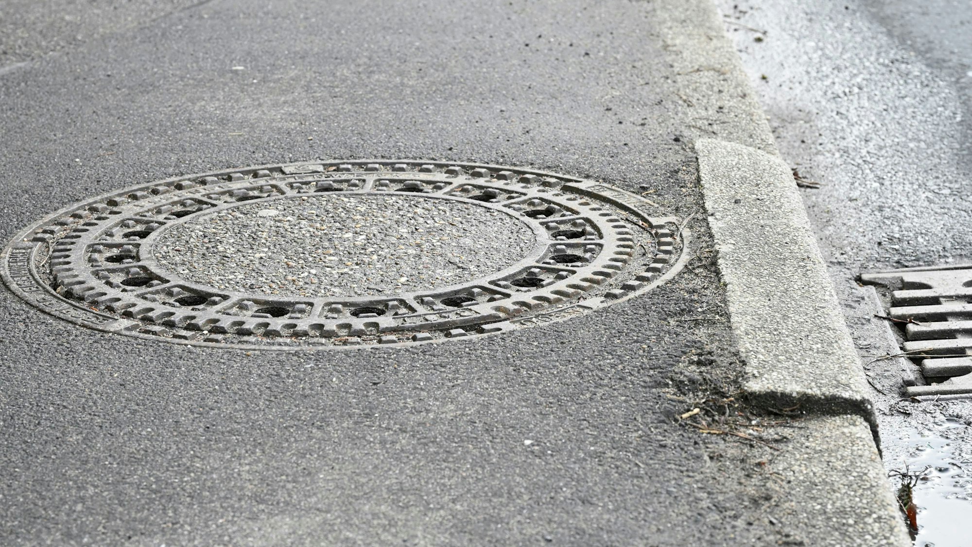 Ein Gehweg mit einem Gullideckel. Ein Stein der Bordsteinkante hat sich gesenkt.