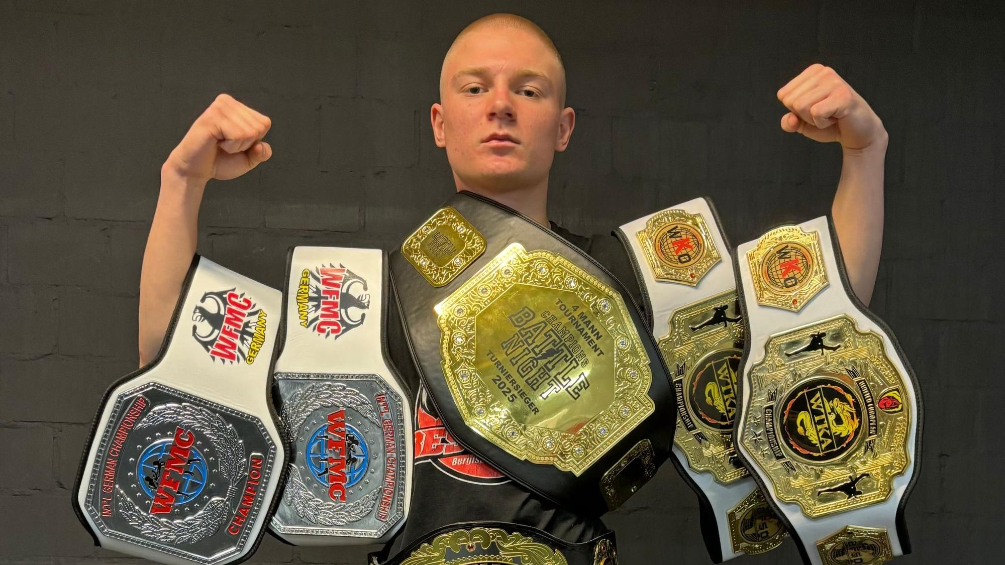 Der Kickboxer trägt seine gewonnenen Gürtel um die Arme geschnallt.