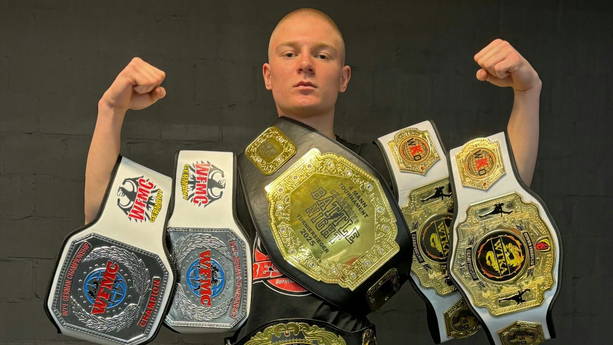 Der Kickboxer trägt seine gewonnenen Gürtel um die Arme geschnallt.