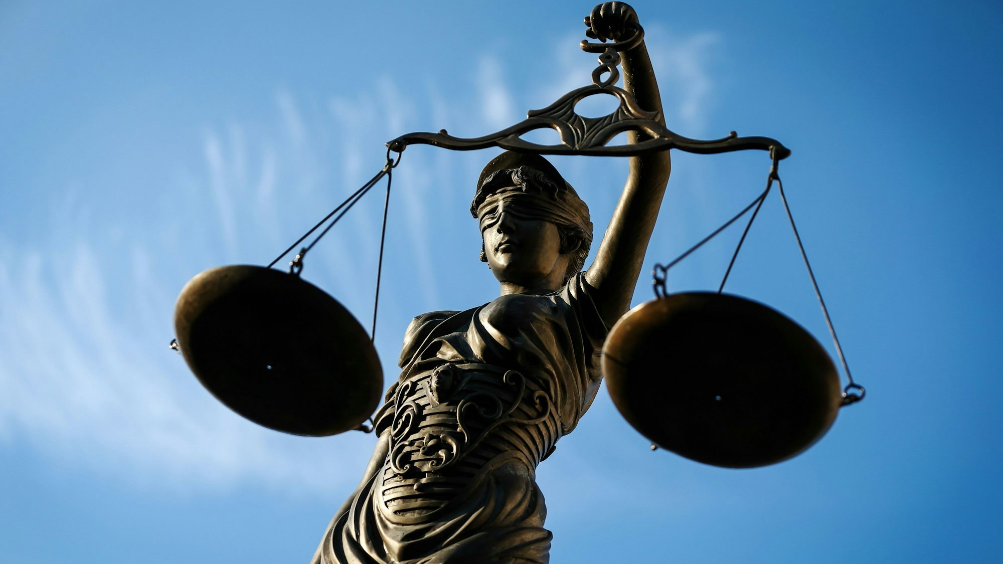 Eine Statue der Justitia aus Bronze, vor blauem Himmel, hält eine Waage in der Hand. (Symbolbild)